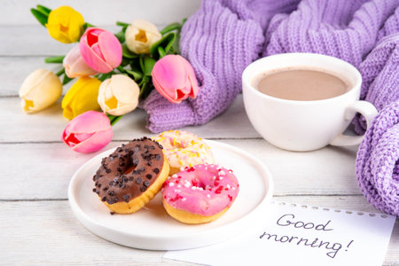 Small sugar glazed donuts with coffee latte cup, tulip flowers, sweater, tulip flower bouquet and note Good Morning. Spring holiday, Mother Day, Woman day, Birthday greeting card backgroundの写真素材