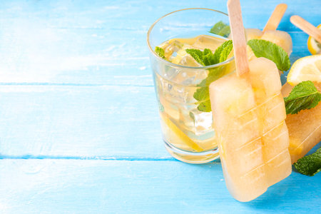 Iced tea or lemonade popsicles, sweet lemon and mint cocktail lollies with cold drink, lemon slices and mint leaves copy spaceの写真素材