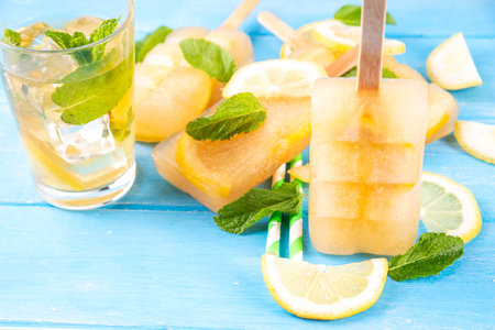 Iced tea or lemonade popsicles, sweet lemon and mint cocktail lollies with cold drink, lemon slices and mint leaves copy spaceの写真素材