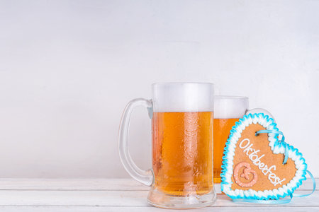 Background for Oktoberfest invitation, menu, greeting card, White wooden table with beer glass mugs, checkered ribbon and heart cookies with Oktoberfest symbols - flower, beer, pretzel top viewの写真素材
