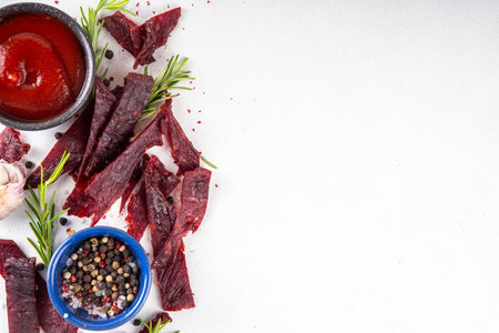 Dried meat snack, jerky beef meat. Healthy beef meat snacks, with sauce and spices on serving board, copy spaceの写真素材