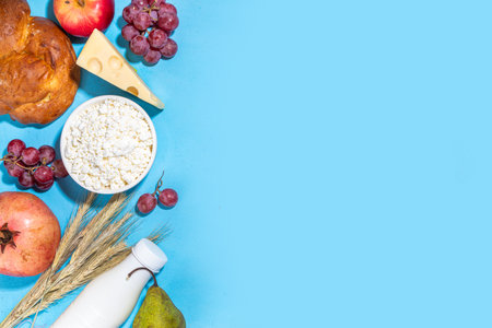 Happy Shavuot greeting card with food Symbols of jewish Shavuot holiday - pomegranate, grapes, apple, sweet challah bread, wheat spikelets, milk, cheese, cottage cheese, on light blue backgroundの写真素材
