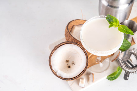 Coconut mint margarita cocktail. Homemade summer cold refreshing coconut milk Lime Margarita with Mint with bar utensils, on white kitchen tableの写真素材