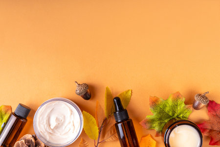 Autumn cosmetics skin care, basic beauty care for fall season. Bottles and jars of face cream, serum, organic autumn natural cosmetics with autumn leaves, cones, acorns on beige backgroundの写真素材
