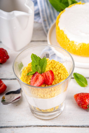 Classic cheesecake in glass, with fresh strawberry and golden cookie crumble. Layered cheesecake dessert with fresh strawberries on white wooden table copy spaceの写真素材