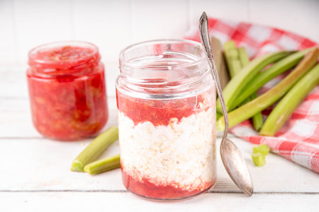 Sweet rhubarb overnight oats in portioned jar. Summer tasty healthy vegan food. Dietary breakfast or snack. Organic rhubarb overnight oats, with rhubarb jam, yogurt, on white wooden table copy spaceの写真素材
