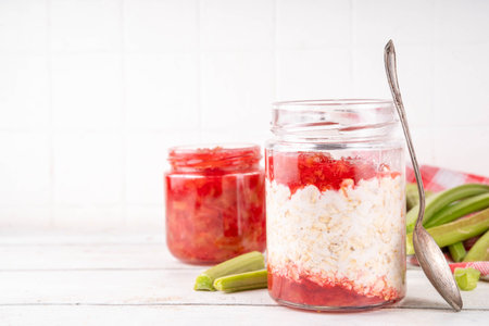 Sweet rhubarb overnight oats in portioned jar. Summer tasty healthy vegan food. Dietary breakfast or snack. Organic rhubarb overnight oats, with rhubarb jam, yogurt, on white wooden table copy spaceの写真素材