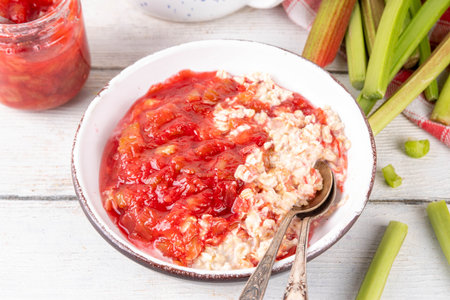 Sweet rhubarb oats in breakfast bowl Summer tasty healthy vegan food. Dietary breakfast or snack. Organic rhubarb overnight oatmeal, with rhubarb jam, yogurt, on white wooden table copy spaceの写真素材
