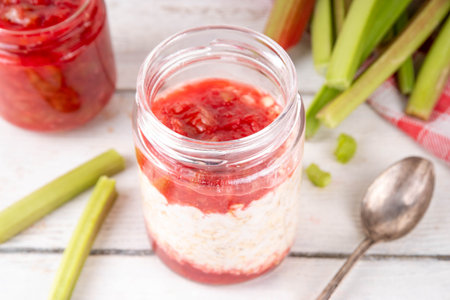 Sweet rhubarb overnight oats in portioned jar. Summer tasty healthy vegan food. Dietary breakfast or snack. Organic rhubarb overnight oats, with rhubarb jam, yogurt, on white wooden table copy spaceの写真素材