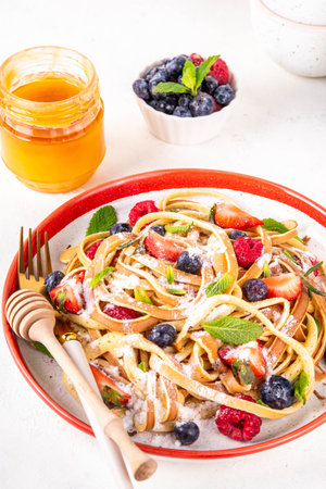Viral trendy spaghetti pancakes with fresh berries, summer sweet breakfast or lunch recipe idea, homemade Pancake make in form of spaghetti with powdered sugar and honey, on white kitchen tableの写真素材