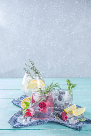 Summer cold drink concept. Fruit and berries gin tonic cocktail, or infused water lemonade mocktails, with fresh blueberry, raspberry, lemon and herbs, blue green old wooden background copy spaceの写真素材