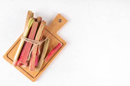 Raw fresh organic rhubarb stems on kitchen table background, bunch of homegrown pink and green rhubarb ready for cooking, on cutting board. Summer harvest, summer food and dessert cooking ingredientの写真素材