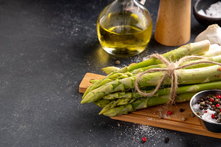 Raw fresh organic asparagus stems on kitchen table background, bunch of homegrown green asparagus ready for cooking, on cutting board. Summer harvest, summer food cooking ingredientの写真素材
