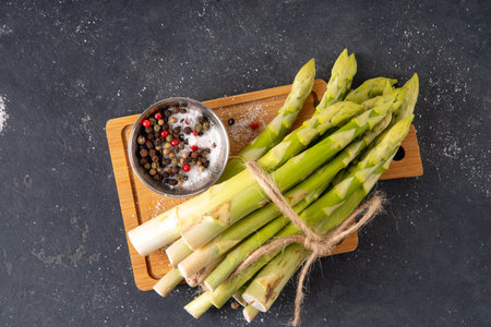 Raw fresh organic asparagus stems on kitchen table background, bunch of homegrown green asparagus ready for cooking, on cutting board. Summer harvest, summer food cooking ingredientの写真素材