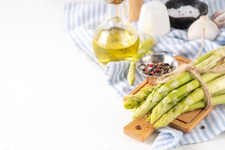 Raw fresh organic asparagus stems on kitchen table background, bunch of homegrown green asparagus ready for cooking, on cutting board. Summer harvest, summer food cooking ingredientの写真素材