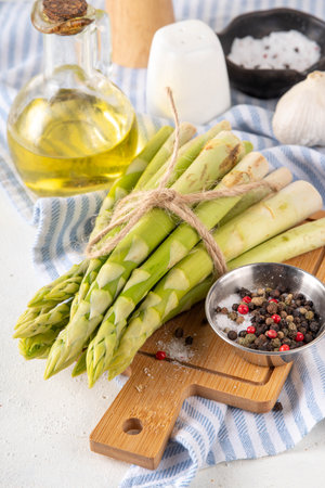 Raw fresh organic asparagus stems on kitchen table background, bunch of homegrown green asparagus ready for cooking, on cutting board. Summer harvest, summer food cooking ingredientの写真素材