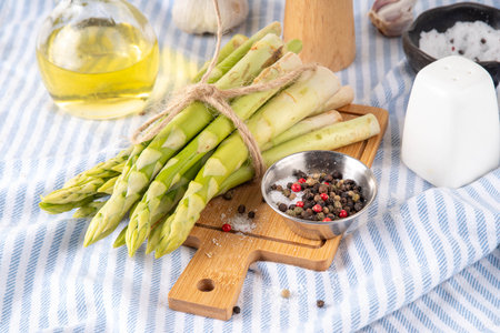 Raw fresh organic asparagus stems on kitchen table background, bunch of homegrown green asparagus ready for cooking, on cutting board. Summer harvest, summer food cooking ingredientの写真素材