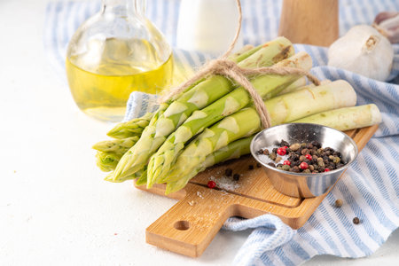 Raw fresh organic asparagus stems on kitchen table background, bunch of homegrown green asparagus ready for cooking, on cutting board. Summer harvest, summer food cooking ingredientの写真素材