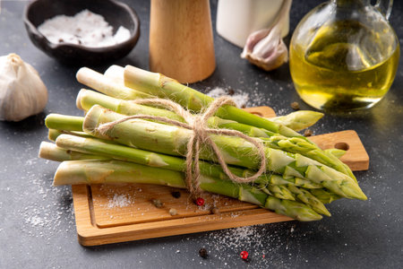 Raw fresh organic asparagus stems on kitchen table background, bunch of homegrown green asparagus ready for cooking, on cutting board. Summer harvest, summer food cooking ingredientの写真素材