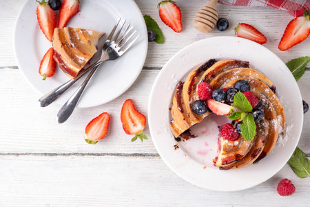 Sweet summer bundt cake with fresh fruit and berry. Traditional round sponge cake, seasonal dessert with strawberry, raspberry, blueberry, honey and sugar sprinkles, white wooden table copy spaceの写真素材