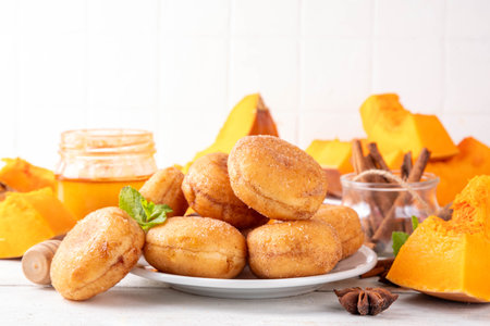 Autumn pumpkin pie donuts with cinnamon sugar sprinkled topping and pumpkin spice filling, on white wooden table with honey and pumpkin squash slices, copy spaceの写真素材