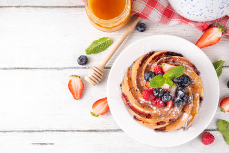 Sweet summer bundt cake with fresh fruit and berry. Traditional round sponge cake, seasonal dessert with strawberry, raspberry, blueberry, honey and sugar sprinkles, white wooden table copy spaceの写真素材