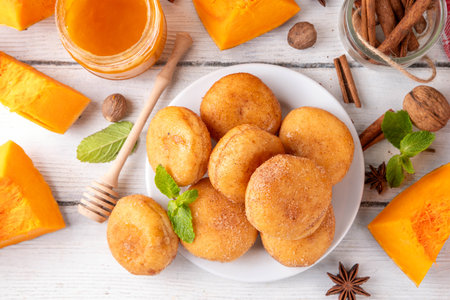 Autumn pumpkin pie donuts with cinnamon sugar sprinkled topping and pumpkin spice filling, on white wooden table with honey and pumpkin squash slices, copy spaceの写真素材