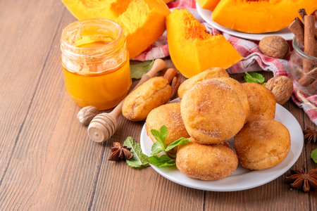 Autumn pumpkin pie donuts with cinnamon sugar sprinkled topping and pumpkin spice filling, on white wooden table with honey and pumpkin squash slices, copy spaceの写真素材
