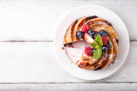 Sweet summer bundt cake with fresh fruit and berry. Traditional round sponge cake, seasonal dessert with strawberry, raspberry, blueberry, honey and sugar sprinkles, white wooden table copy spaceの写真素材