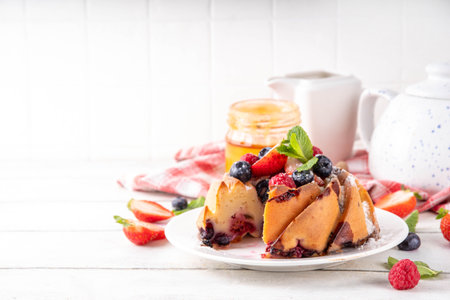 Sweet summer bundt cake with fresh fruit and berry. Traditional round sponge cake, seasonal dessert with strawberry, raspberry, blueberry, honey and sugar sprinkles, white wooden table copy spaceの写真素材