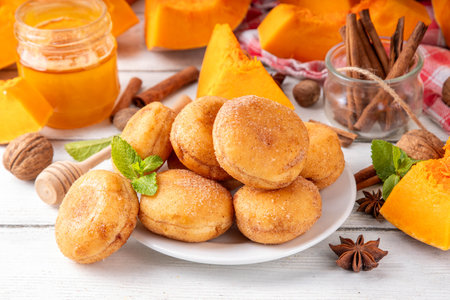 Autumn pumpkin pie donuts with cinnamon sugar sprinkled topping and pumpkin spice filling, on white wooden table with honey and pumpkin squash slices, copy spaceの写真素材