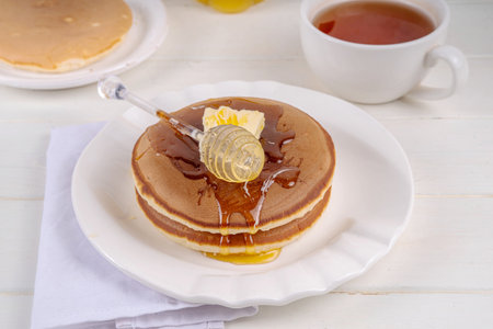 Stack of fresh baked homemade breakfast pancakes with butter and honey or maple syrup drizzles on white wooden tableの写真素材
