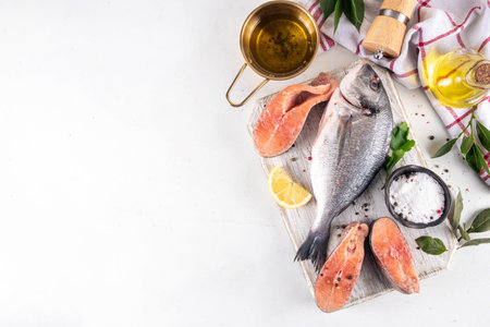 Raw fish and seafood cooking background, various fresh whole and sliced fish with spices, lemon, olive oil for preparation dinner, white table background copy spaceの写真素材
