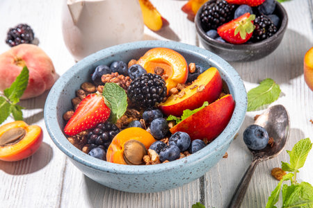 Granola breakfast with fruit and berry, summer whole grain tasty breakfast bowl with a lot of fruit and berries, with milk jug on white wooden tableの写真素材