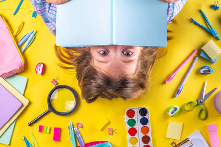 Cute emotional girl ready to back to school with various school supplies, education accessories on bright yellow backgroundの写真素材