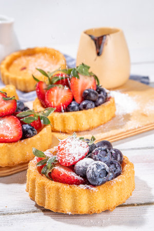 Sponge mini tart cakes with summer berry. Portioned vanilla dessert cups with fresh strawberry, blueberry, raspberry, on white wooden background copy spaceの写真素材