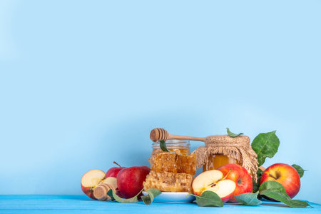 Jewish holiday Rosh Hashanah or apple feast day concept, with red apples, apple leaves, honey in jar and honeycombs light blue wooden background copy space aboveの写真素材