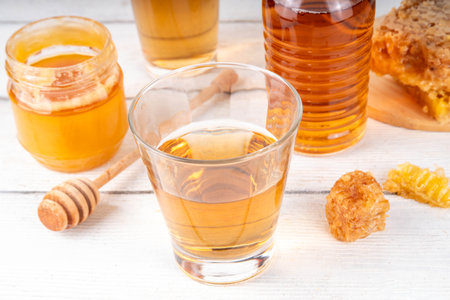 Homemade honey alcohol drink mead, golden amber honey liqueur beverage with honeycomb, honey jar and dipper, copy spaceの写真素材