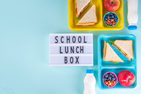 Healthy school meal, children packed lunch box with fruit, berry, nuts and sandwich with vegetables. Kids diet snack food with education school supplies, bright blue background top view copy spaceの写真素材