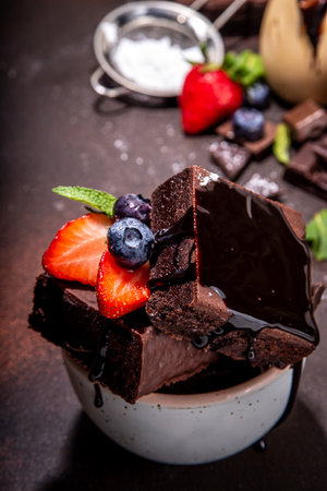 Dark chocolate brownies with berries. Stack of homemade brownie cake cookies with chocolate sauce drizzled on it and fresh strawberry, blueberry, on dark background copy spaceの写真素材