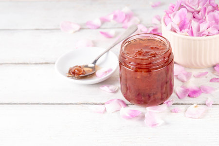 Rose petals jam, sweet tasty flower dessert, homemade confiture preserves with organic dessert roses petals, sugar and honey, in small jar on white table.  Alternative medicine, remedies for sore throats and coldsの写真素材
