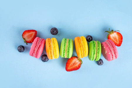 Bright and colorful sweet macaroons dessert with fresh berries. Pink, orange, yellow and pistachio green tasty macaron cookies on light blue background copy spaceの写真素材