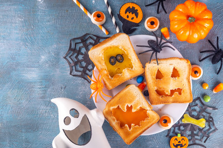 Funny kids food for Halloween, snack or brunch sandwiches with toasted bread, cheese in shape of Halloween traditional monsters - pumpkin jack lantern, ghost, bat, with holiday decor on blue tableの写真素材