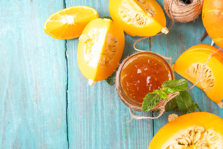 Golden pumpkin jam preserves. Sweet pumpkin and orange marmalade or confiture in small jar, with sliced pumpkin and mint on wooden kitchen table, copy spaceの写真素材