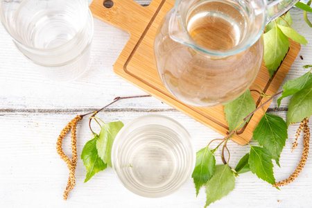 Birch sap in jar and glass, freshly made organic birch juice, sweet natural drink, on white wooden background with birch tree twigsの写真素材