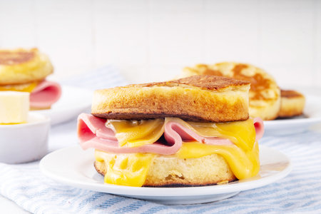 Breakfast crumpet sandwich, british pancake scones burger with cheese and ham, on itchen table, with stack of crumpets and butterの写真素材