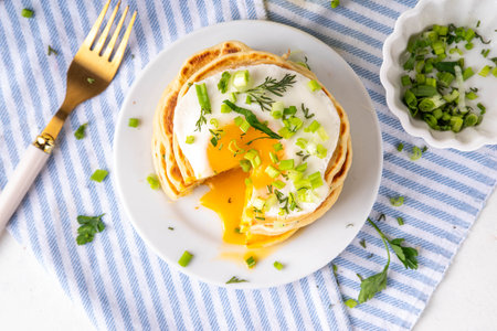 Tasty savory breakfast pancakes with spring green onion and fried eggs. Stack or delicious non-sweet pancakes with scallons, parsley and sunny side up eggs, on white kitchen table copy spaceの写真素材