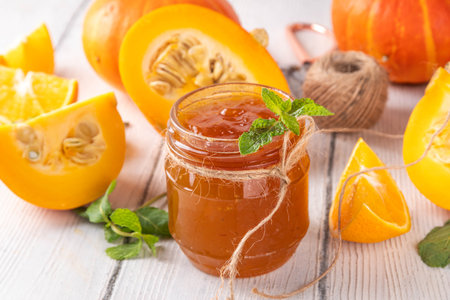 Golden pumpkin jam preserves. Sweet pumpkin and orange marmalade or confiture in small jar, with sliced pumpkin and mint on wooden kitchen table, copy spaceの写真素材