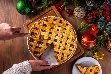 Traditional British Christmas mince pie. Homemade sweet mincemeat tart cake, filled with spiced dried fruit, nuts and apples, on cozy wooden table with  with Christmas tree and decorationの写真素材