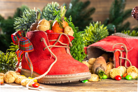 Sinterklaas, Saint Nicholas day background. Little kid red shoe with carrots and sweets, trooigoed, pepernoten, candy. Dutch Christmas holiday on cozy wooden background.の写真素材